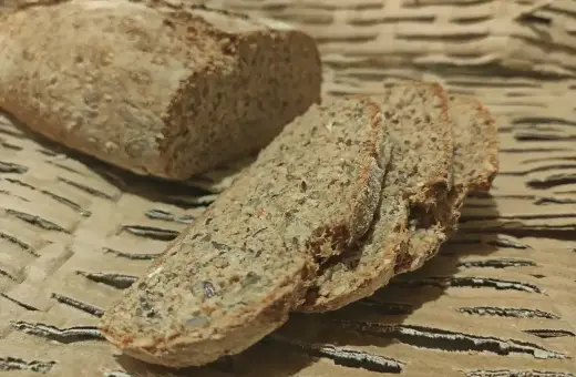 Chleb orkiszowy, pokrojony na kromki, z widocznymi ziarnami, leży na falistej tekturze.
