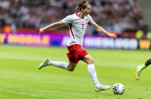 Jakub Kamiński w akcji, biegnie z piłką na boisku. Jego obecne drużyny to reprezentacja Polski i VfL Wolfsburg.