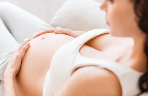 Kobieta w 7 miesiącu ciąży delikatnie głaszcze swój brzuszek.