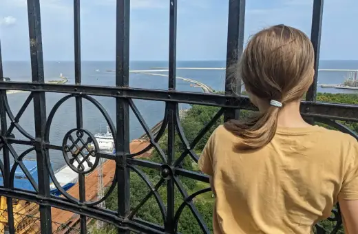 Dziewczynka podziwia widok z najwyższej latarni morskiej w Polsce. Widać morze, port i statki.
