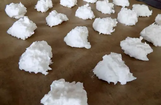 Na papierze do pieczenia ułożone są białe, puszyste kupki, które wyglądają jak najprostsze kokosanki.