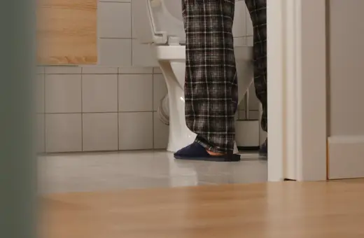 Osoba w piżamie stoi przy toalecie, widać jej nogi i kapcie. Czyżby pojawiły się bąbelki w moczu?