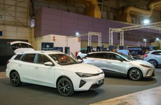 Białe kombi MG5 z otwartą klapą bagażnika i srebrny SUV na wystawie samochodowej.