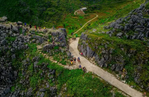 Grupa rowerzystów na malowniczej trasie Ha Giang Loop, wśród skalistych zboczy i zielonych tarasów.