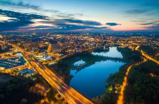 Widok z lotu ptaka na miasto nocą, z oświetloną autostradą i **trzech stawów** odbijających światła miasta.