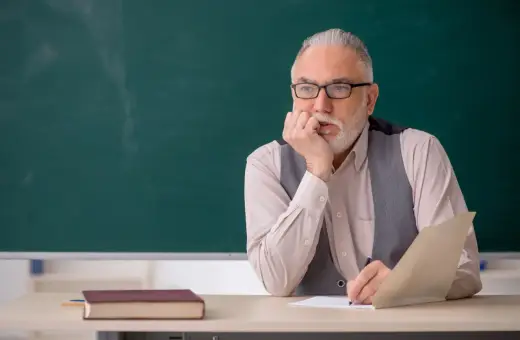 Starszy nauczyciel zamyślony nad dokumentami, być może planuje swoją sześciomiesięczną odprawę emerytalną.