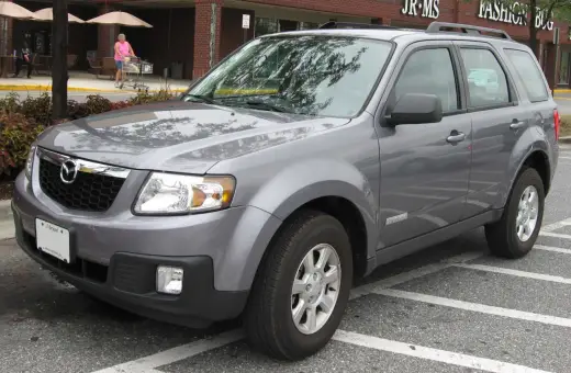 Szary Mazda Tribute zaparkowany na parkingu przed sklepem.