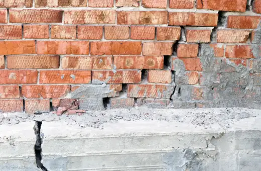 Uszkodzona ceglana ściana z pękniętym betonowym fundamentem. Podbijanie fundamentów cena – pilna naprawa.