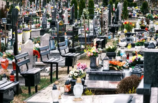 Ławki na cmentarzu, przygotowane na wizytę bliskich. Wiele zniczy i kwiatów świadczy o pamięci.