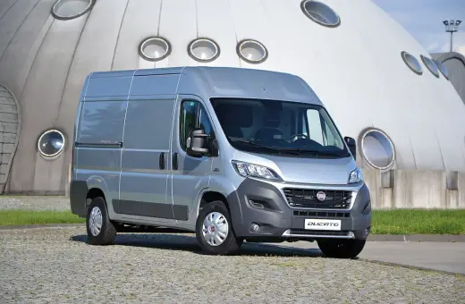 Srebrny Fiat Ducato 2.3 Multijet zaparkowany przed futurystycznym budynkiem z okrągłymi oknami.