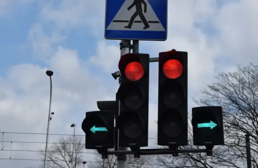 Sygnalizacja świetlna: czerwone światła dla jazdy prosto, zielona strzałka w lewo. Czy na strzałce w lewo można zawracać? Znak przejścia dla pieszych.