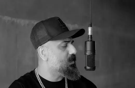 Artysta w czapce z daszkiem i łańcuchem na szyi nagrywa utwór rnb przy mikrofonie.