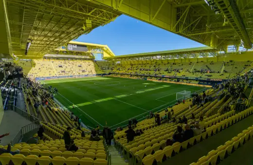 Stadion Villarreal, wypełniony żółtymi siedzeniami, z zieloną murawą i błękitnym niebem.