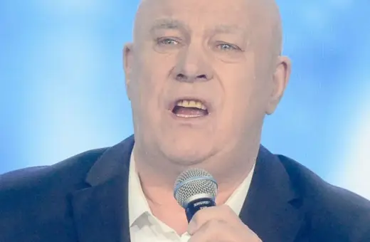 Ryszard Rynkowski śpiewa, trzymając mikrofon. Jego charakterystyczne utwory poruszają serca słuchaczy.