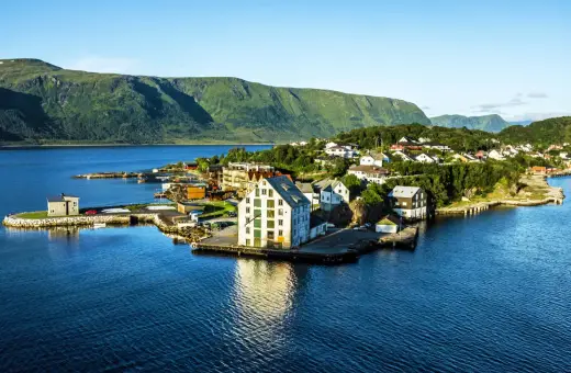 Malowniczy widok na Ålesund Vigra z domkami nad wodą i zielonymi wzgórzami w tle.