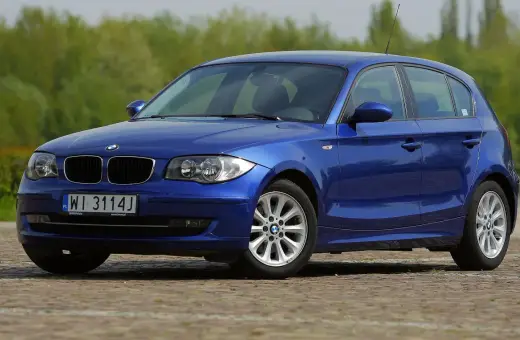 Niebieskie BMW 118i na tle zieleni. Elegancki hatchback z polskimi tablicami rejestracyjnymi WI 3114J.