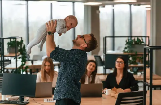 Szczęśliwy ojciec podrzuca dziecko w biurze, podczas gdy koleżanki pracują. Czy urlop wychowawczy wlicza się do stażu pracy?