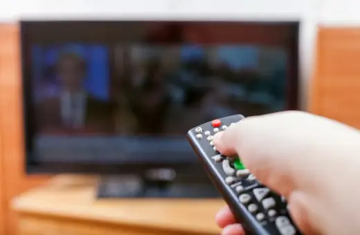 Dłoń z pilotem przed telewizorem, być może to już koniec abonamentu rtv i czas na zmiany.