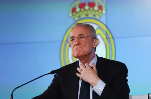 Florentino Pérez, prezes Realu Madryt, w garniturze, z ręką na szyi, na tle logo klubu.