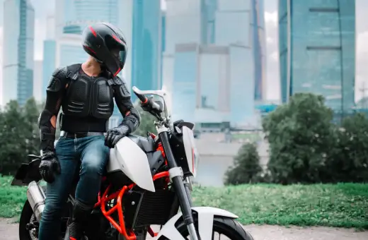 Motocyklista w zbroi ochronnej siedzi na motocyklu na tle wieżowców.
