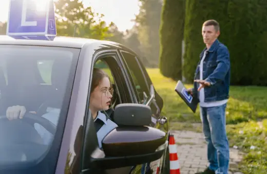 Młoda kursantka za kierownicą samochodu z literą "L", instruktor obok z tabliczką. Czy kurs na prawo jazdy przepada?
