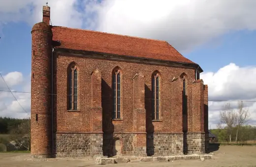 Gotycka budowla z cegły, przypominająca dawną warownię templariuszy, z charakterystyczną okrągłą wieżą i strzelistymi oknami.