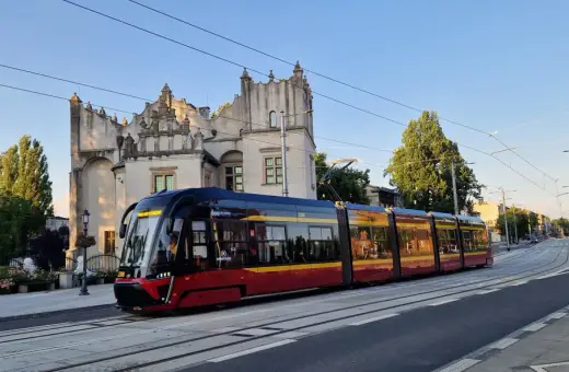 Nowoczesny tramwaj pabianice z czerwono-żółtymi pasami jedzie w stronę zabytkowego budynku.
