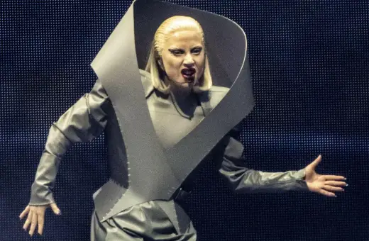Lady Gaga w szarym, futurystycznym stroju na koncercie w Polsce, z charakterystycznym kołnierzem i makijażem.
