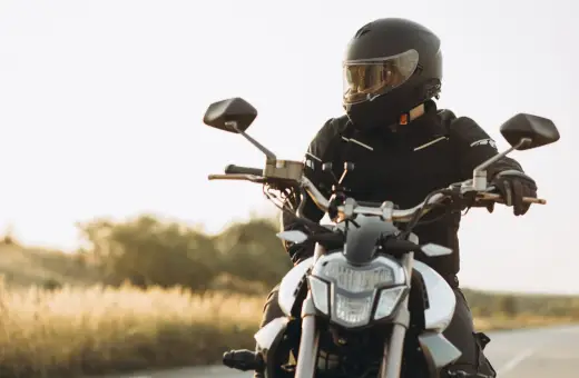 Motocyklista w kasku i kurtce siedzi na motocyklu na tle krajobrazu.