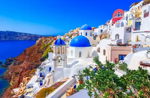 Santorini wakacje: białe domy z niebieskimi kopułami na zboczu klifu nad lazurowym morzem. Idealne miejsce na wymarzone wakacje.