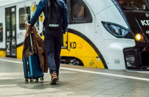 Podróżny z walizką i kurtką idzie na pociąg. Może to być podróż z Warszawy do Gdyni.