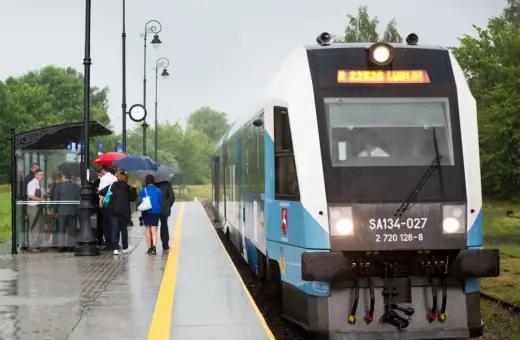 Szynobus Lublin - Zamość trasa. Pasażerowie z parasolami czekają na deszczowy dzień na peronie.