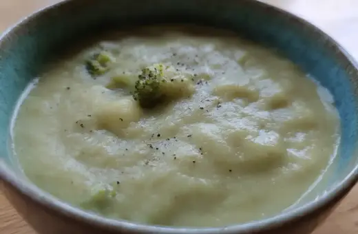 En krämig potatis och broccolisoppa, toppad med lite svartpeppar, serveras i en blå kantad skål.