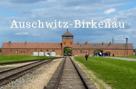 Brama obozu Auschwitz-Birkenau, gdzie jest to miejsce pamięci. Tłum zwiedzających podąża torami kolejowymi.