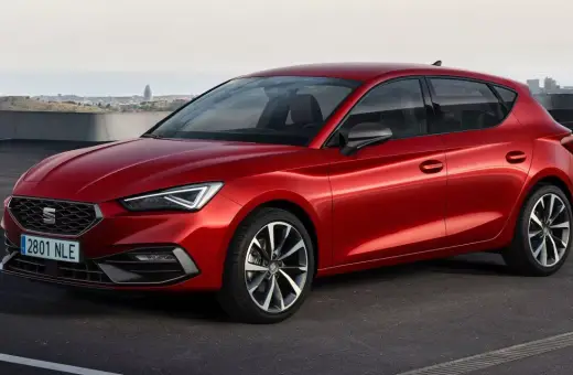 Czerwony Seat Leon, auto pochodzenia hiszpańskiego, zaparkowany na tle miasta.