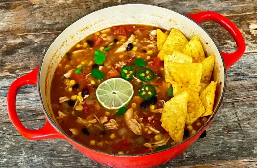 Prawdziwa zupa meksykańska w czerwonym garnku, pełna kurczaka, fasoli, kukurydzy, z limonką i jalapeño. Chrupiące nachos na wierzchu.