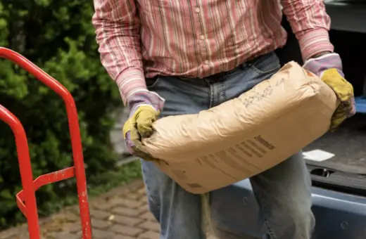Mężczyzna w rękawicach niesie worek cementu. Zastanawia się, ile piasku na 25 kg cementu będzie potrzebne do budowy.