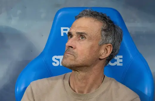 Luis Enrique, kto jest trenerem PSG, siedzi na niebieskiej ławce, zamyślony.