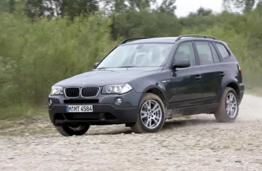 Ciemnoszary BMW X3 2024 na szutrowej drodze, otoczony zielenią.