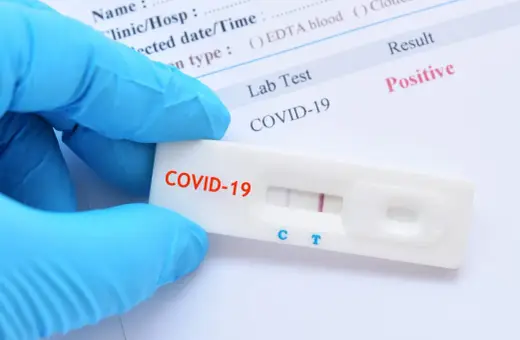 Ręka w niebieskiej rękawiczce trzyma test antygenowy COVID-19 z dwoma widocznymi liniami, co oznacza pozytywny wynik.