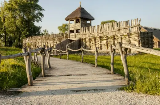 Drewniana kładka prowadzi do grodziska z wieżą obronną. To fragment szlaku piastowskiego, gdzie historia ożywa.