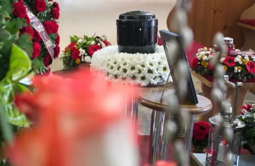 Urzna z prochami, otoczona kwiatami, obok wieńca z czerwonych róż. Czy kremacja boli? To pytanie, na które odpowiedź zna tylko zmarły.