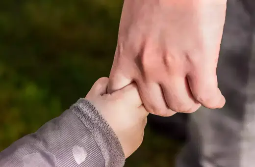 Dłoń dorosłego, opiekuna prawnego, mocno trzyma dłoń dziecka.