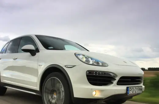 Biały Porsche Cayenne 2025 pędzi po drodze, chmury na niebie sugerują dynamiczną podróż.