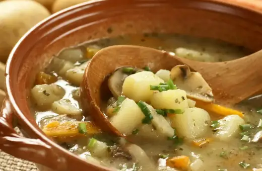 Zupa ziemniaczana przepis babci. Aromatyczna, sycąca zupa z ziemniaków, marchewki i grzybów, podana w glinianej misce z drewnianą łyżką.