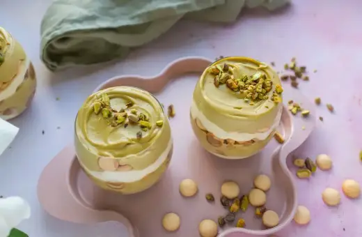 Dwa pucharki z kremem pistacjowym z mascarpone, udekorowane posiekanymi pistacjami.