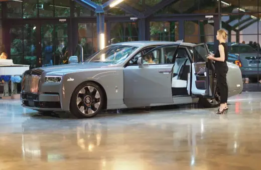 Elegancki szary Rolls-Royce Phantom z otwartymi drzwiami, obok którego stoi kobieta. Poznaj jego wyjątkową rolls royce phantom cena.