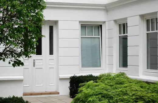 Boniowanie elewacji domu podkreśla jego klasyczny charakter. Białe drzwi i okna, otoczone zielenią, tworzą elegancką całość.