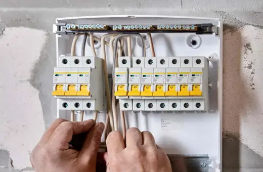 Ręce elektryka podłączają przewody do skrzynki z bezpiecznikami. To właśnie wlz co to za instalacja?