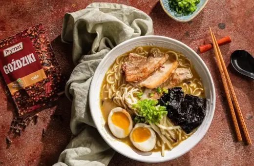 Jak zrobić ramen? Aromatyczny bulion, makaron, jajko na pół, plastry boczku i nori. Obok paczka goździków Prymat.